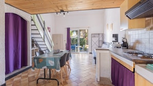 Una cocina moderna con techo de madera, un área de comedor con mesa y sillas, y una escalera que lleva a un espacio al aire libre.