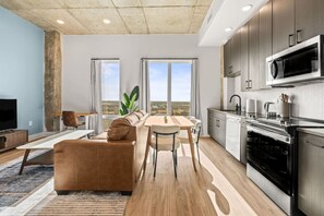 Um apartamento moderno com sala de estar, área de jantar e cozinha. Possui uma janela grande, televisão de tela plana e forno embutido.
