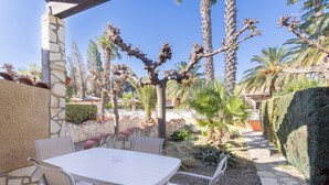 A patio with a table and chairs, surrounded by palm trees and a stone wall. - Holiday Home 'La Capelle 4 Persons 880' with Shared Pool, Wi-Fi and Air Conditioning (Roquefort-des-Corbières)