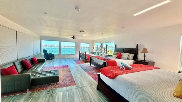 A spacious bedroom with a large bed, a sofa, and a chair, all facing a large window with a view of the sea.
