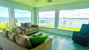 A spacious living room with a large window offering a view of the water and distant buildings.