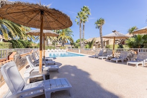 A poolside area with lounge chairs, umbrellas, and palm trees.