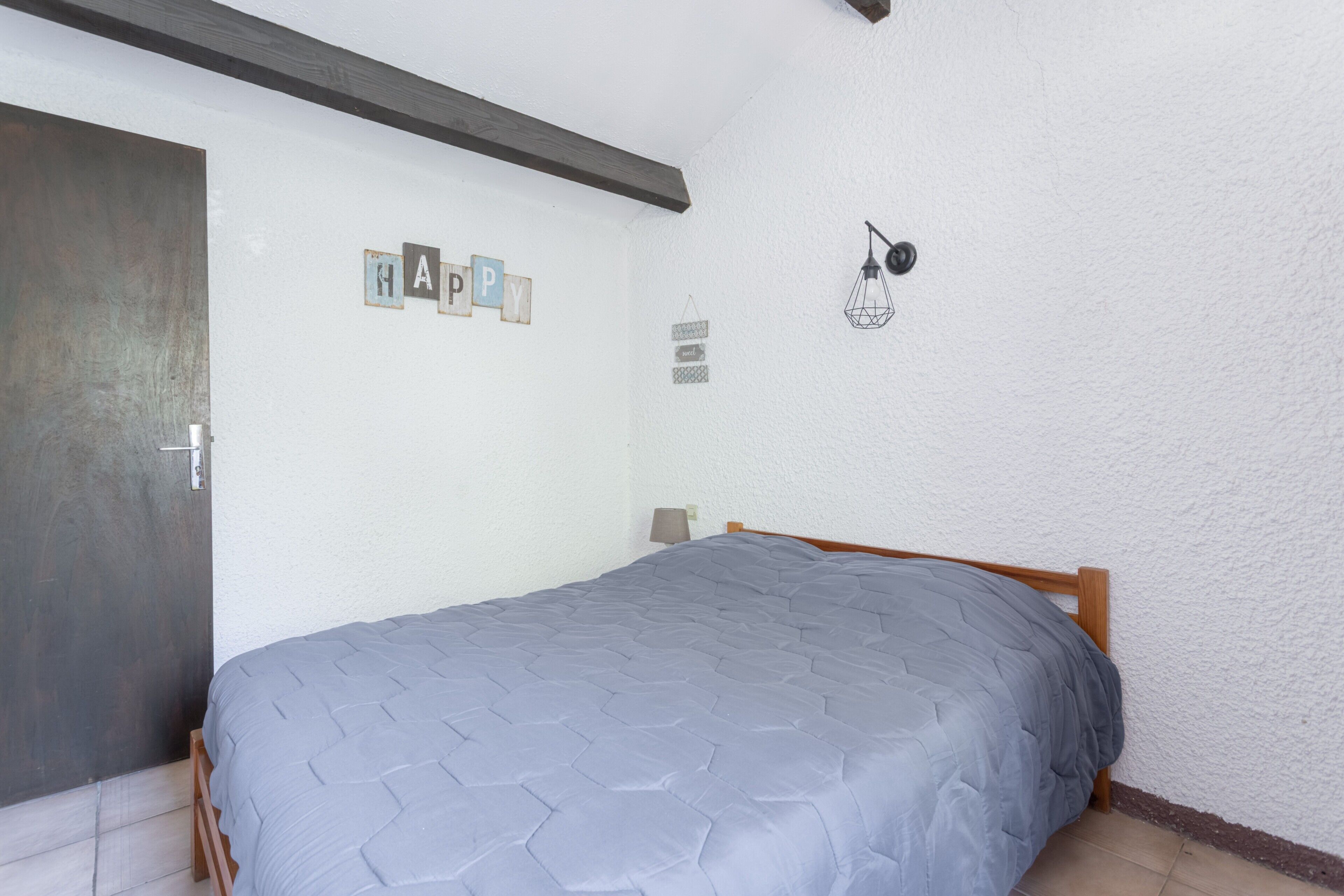 Une chambre avec un lit, une porte, un mur orné d’une décoration représentant le mot « JOIE », et un luminaire suspendu.