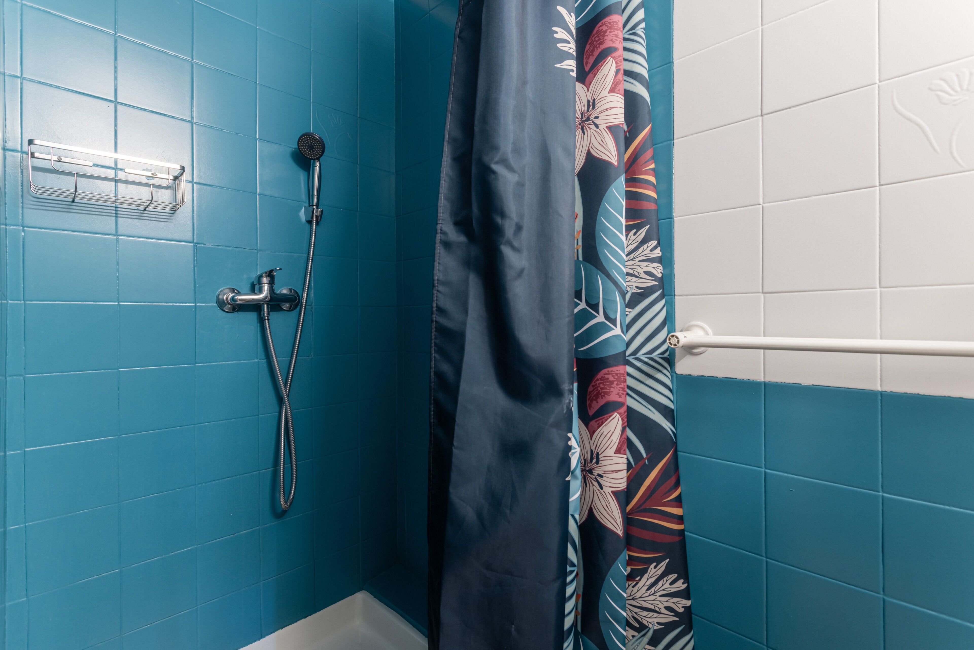 Ein Badezimmer mit blauen Fliesen, einer Dusche inklusive Handbrause, einem Handtuchhalter und einem Duschvorhang mit Blumenmuster.
