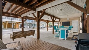 A covered outdoor area with a wooden bench, a table with chairs, and a grill.