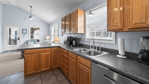 A modern kitchen with wooden cabinets, a granite countertop, a built-in dishwasher, and a window with blinds.