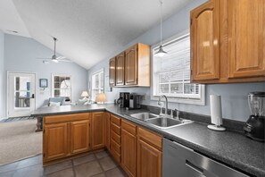 A modern kitchen with wooden cabinets, a granite countertop, a built-in dishwasher, and a window with blinds.
