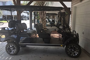 Een overdekte parkeerplaats met een golfkarretje, palmbomen en een garagepoort.