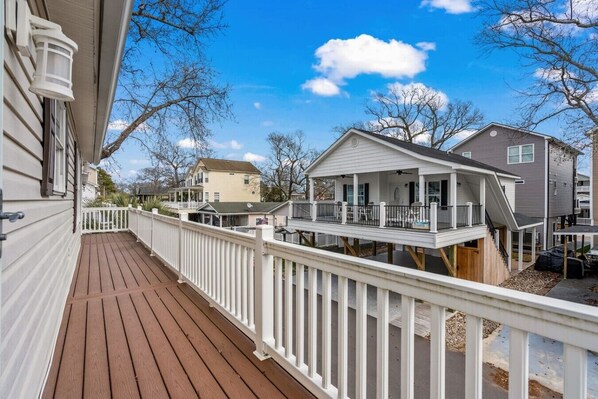 A residential area with a wooden deck, white railings, and houses with balconies.