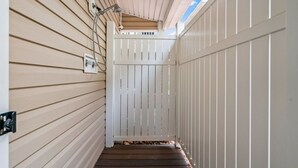 A narrow wooden pathway leading to a white gate, with a ceiling and a light fixture above.