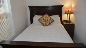 Una cama bien hecha con un cojín floral, una lámpara de noche y un cabecero de madera oscura.