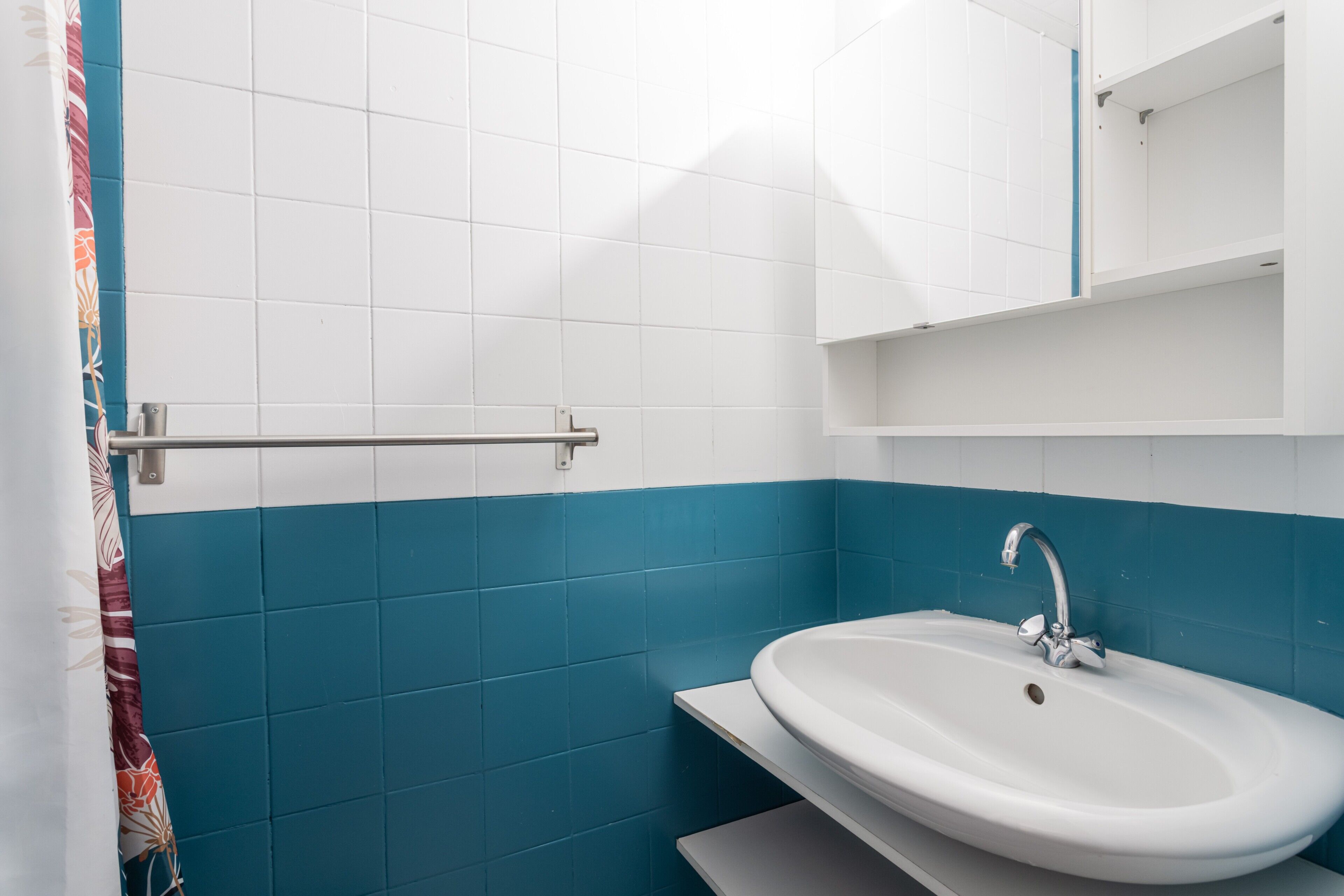 Un baño con baldosas blancas y azules, un lavamanos blanco, un espejo y un perchero para toallas.