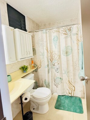 A bathroom with a toilet, a sink, a cabinet, a shower curtain with sea life patterns, and a green bath mat.