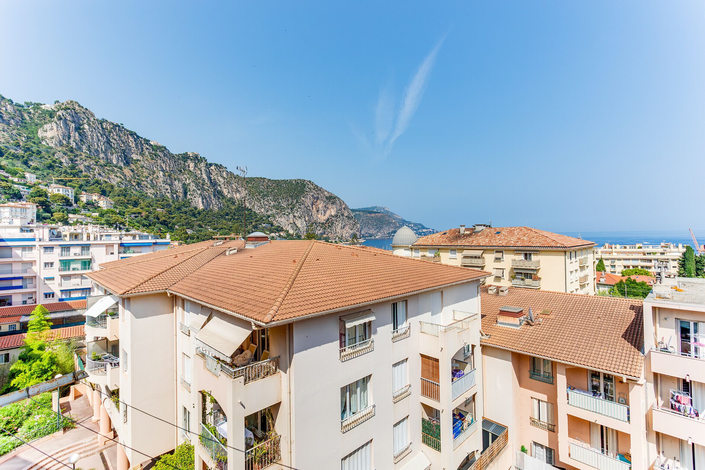 Zona residencial costera con edificios de varios pisos, balcones y montañas al fondo.