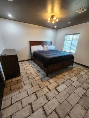 A bedroom with a brick-patterned floor, a wooden bed, a nightstand, and a window with blinds. - The Compound in downtown (Phoenix)