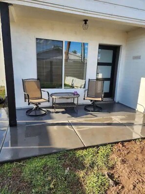 Ein überdachter Patio-Bereich mit zwei Stühlen und einem kleinen Tisch, einem Fenster und einer Tür.