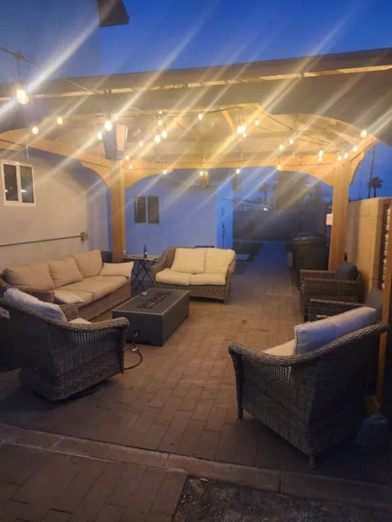 Un espacio al aire libre con patio, muebles de mimbre e iluminación con luces colgantes.