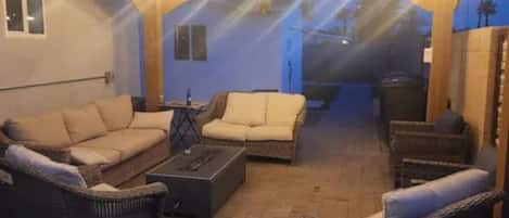 Un espacio al aire libre con patio, muebles de mimbre e iluminación con luces colgantes.