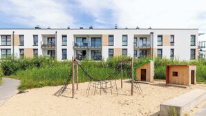 A modern apartment building with multiple balconies, a playground with a hammock, and a small wooden structure.