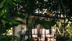 A modern outdoor seating area with a wooden deck, surrounded by lush greenery and a white building with large windows.