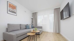 Una sala de estar moderna con un sofá gris, una mesita redonda y un televisor montado en la pared.