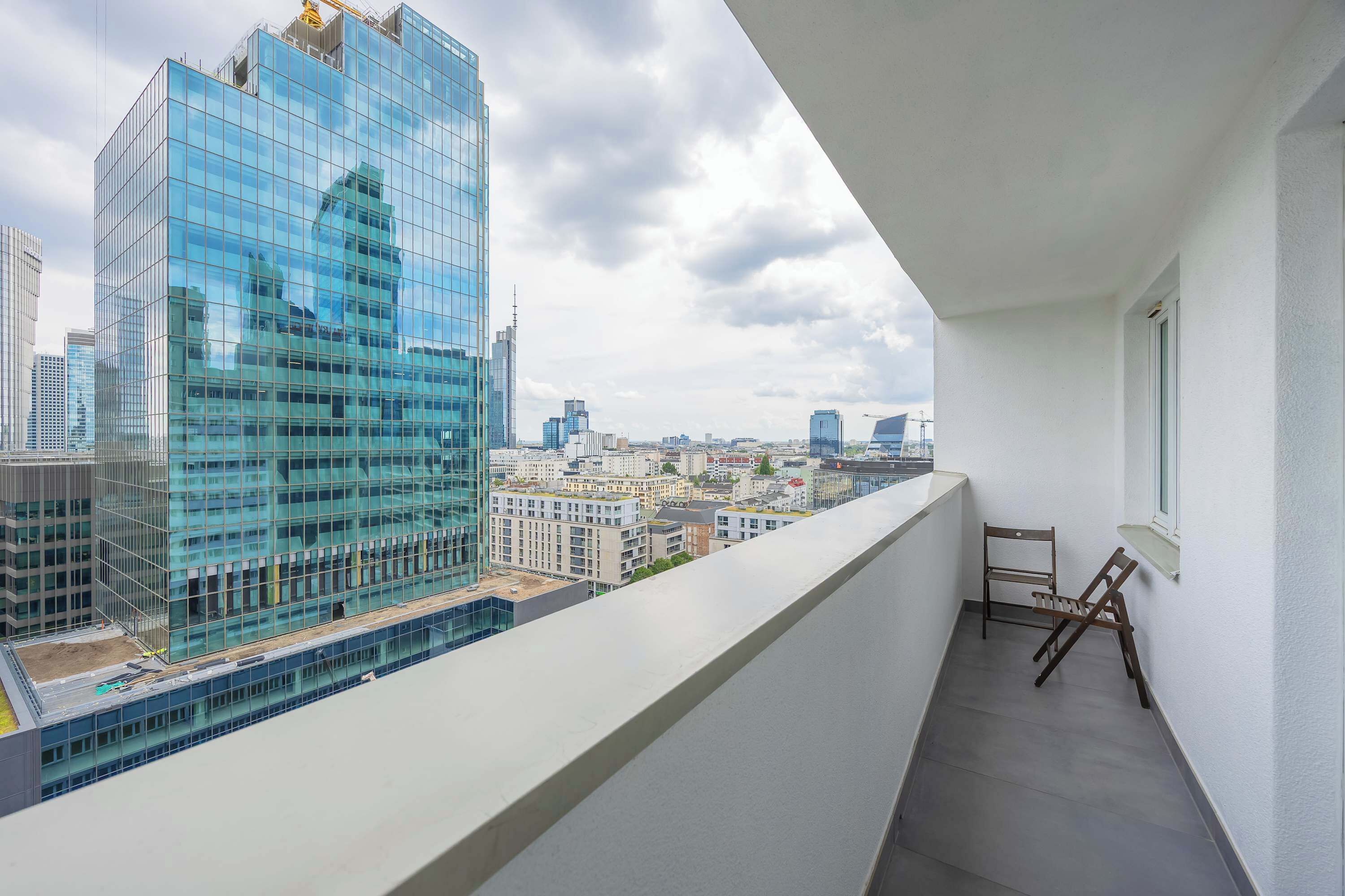 En balkon med udsigt over en moderne glasbygning og det omkringliggende bybillede.
