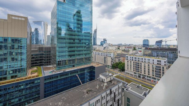 Un edificio de gran altura con fachada de vidrio, rodeado de otros edificios modernos y una grúa de construcción al fondo.