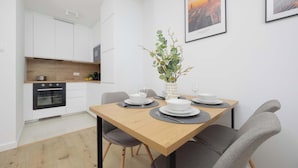 Una cocina moderna con armarios blancos, horno empotrado y comedor con mesa de madera preparada para cuatro comensales.