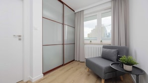 Una habitación moderna con puerta de vidrio corredera, un sofá gris, una mesita con una planta y vistas de la ciudad a través de la ventana.