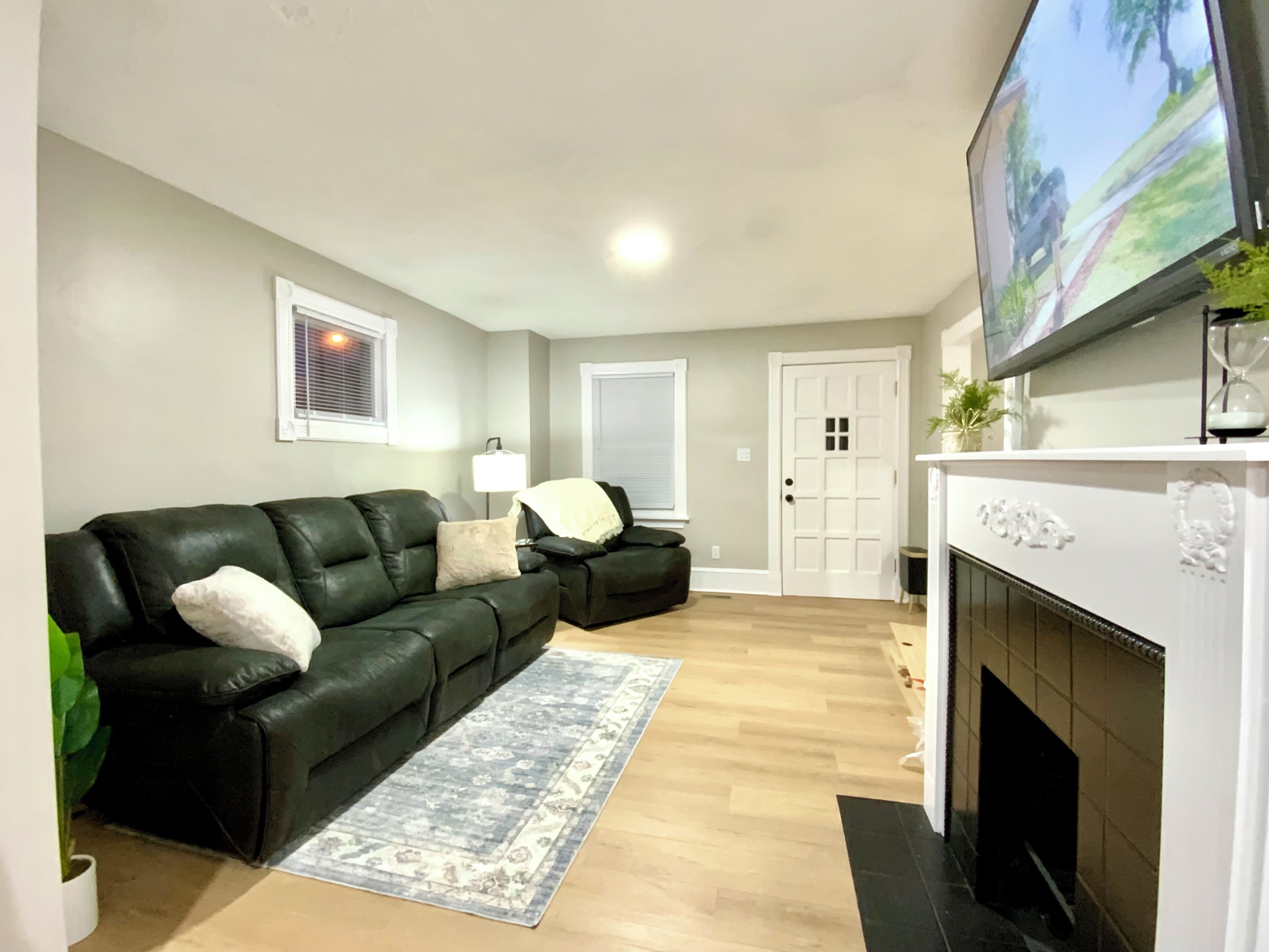 A living room with a black leather sofa, a fireplace, and a television mounted above it.