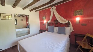 A room with a large bed, a mirror, a red wall, and a wooden ceiling.