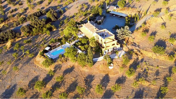 An aerial view of a property with a swimming pool, a covered patio, and a landscaped garden.