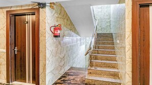 Un couloir d’hôtel aux murs de marbre, une porte en bois portant l’inscription « 207 », un extincteur fixé au mur et une rambarde en verre sur un escalier.
