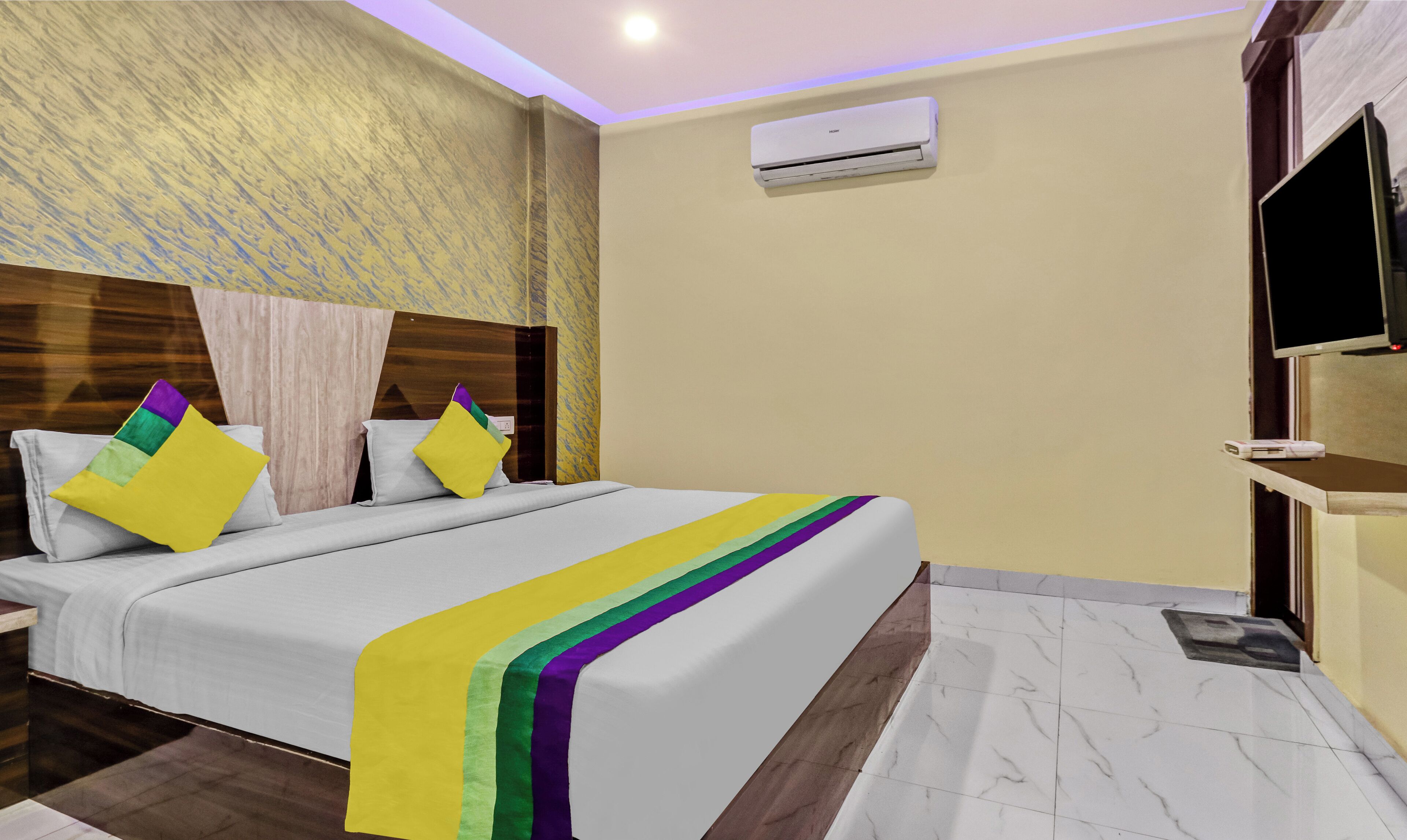 A hotel room with a bed, pillows, a TV, and an air conditioning unit.