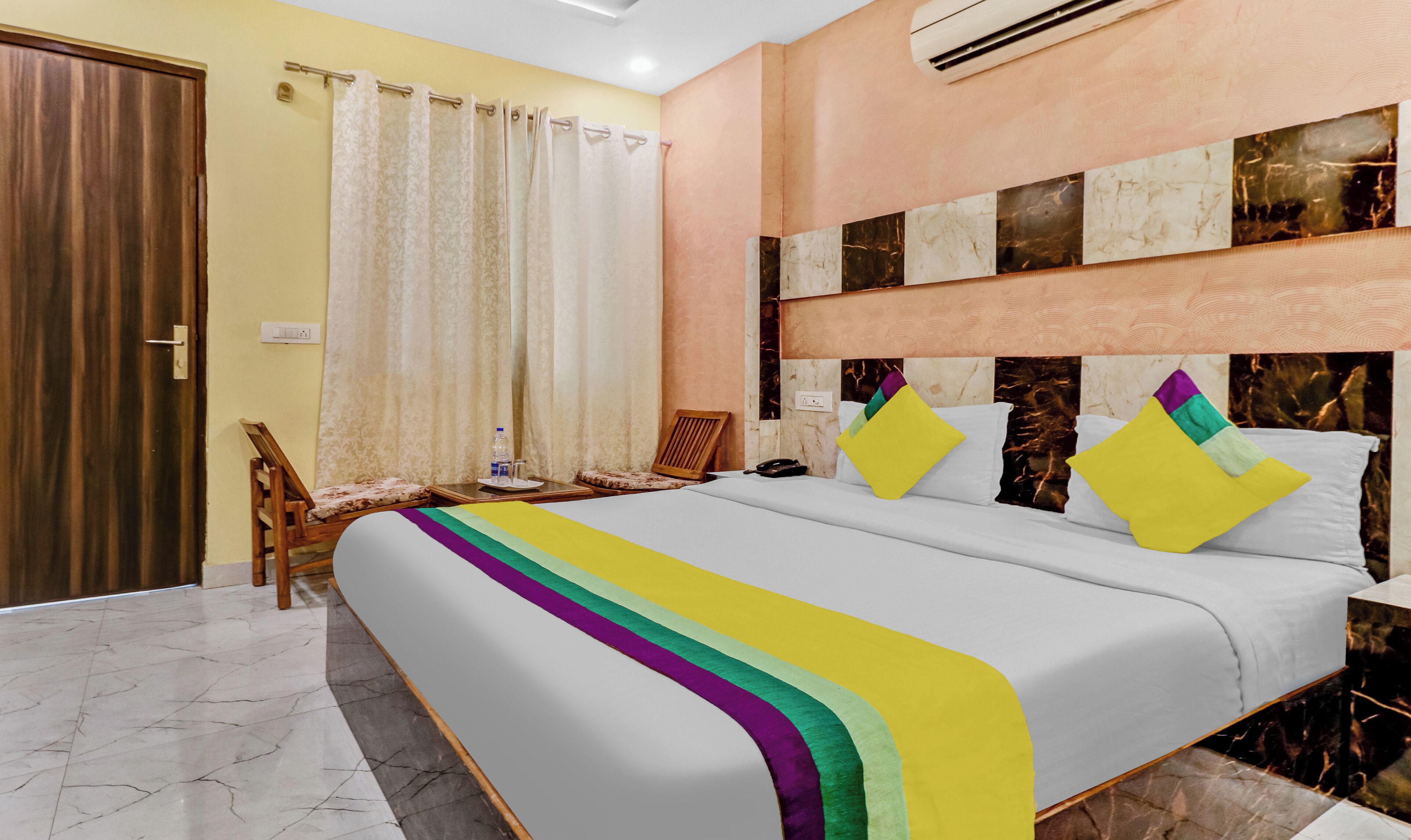 Quarto de hotel com cama, cadeira, mesa de cabeceira e banheiro com cortina.