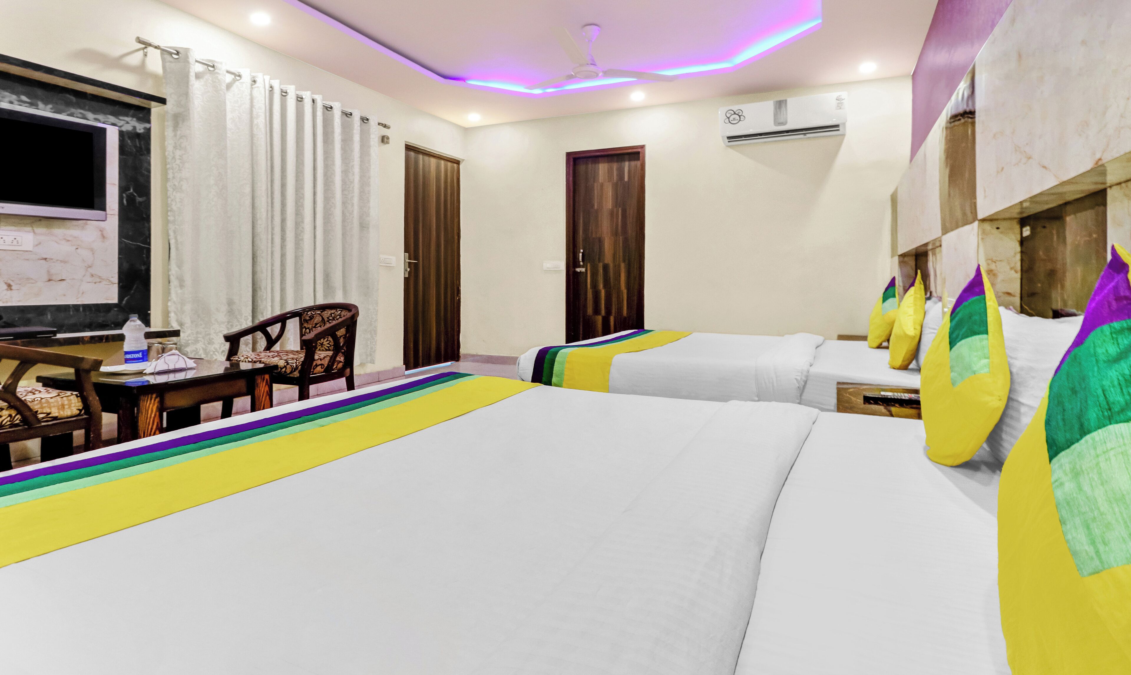 A hotel room with two beds, a desk with a chair, a TV, and an air conditioning unit.