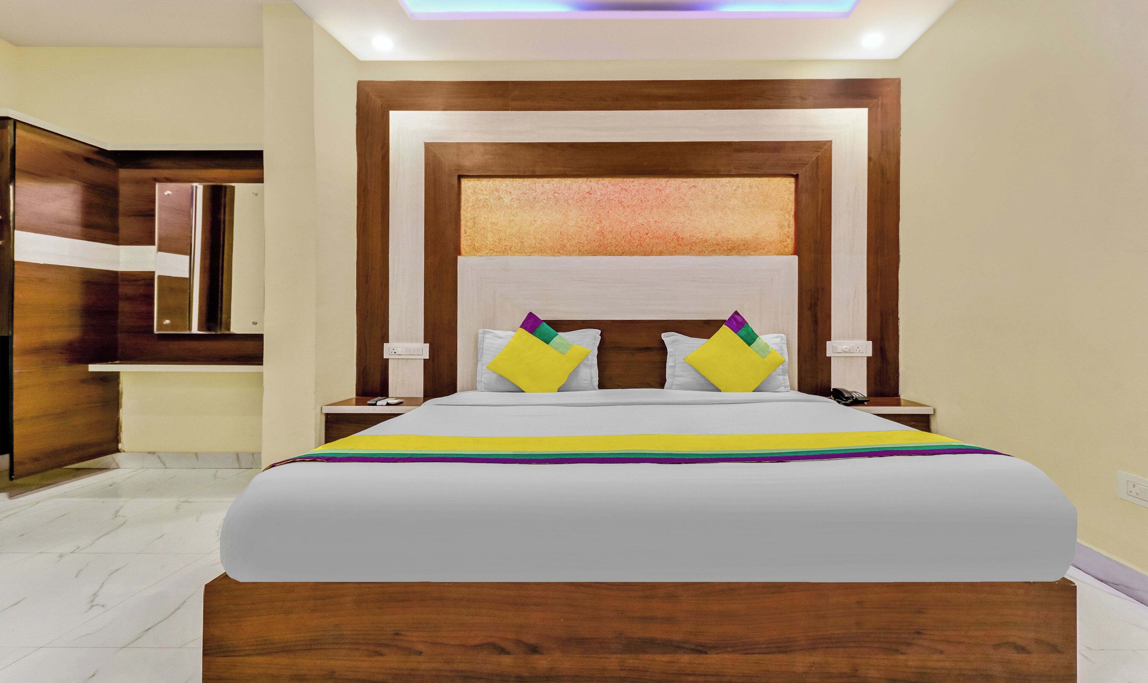 A hotel room with a large bed, wooden headboard, and a nightstand with a phone.