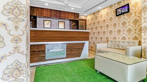 Un espace d’accueil d’hôtel au design moderne, comprenant un comptoir d’accueil, un canapé et un téléviseur fixé au mur.