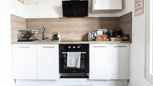 A modern kitchen with white cabinets, a black stove, and a wooden backsplash. - Comfortable studio near Paris-Orly airport (Villeneuve-le-Roi)