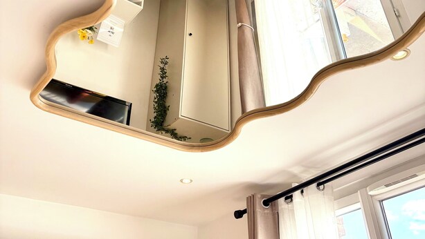 A room with a large mirror reflecting a staircase, a flat-screen TV, and a window with curtains. - Comfortable studio near Paris-Orly airport (Villeneuve-le-Roi)