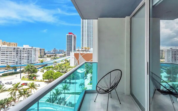 A balcony with a view of a cityscape, a chair, and a pool. - Sian Ocean Residence Komffy - S (Hollywood)