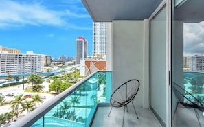 Un balcón con vistas a un paisaje urbano, una silla y una piscina.