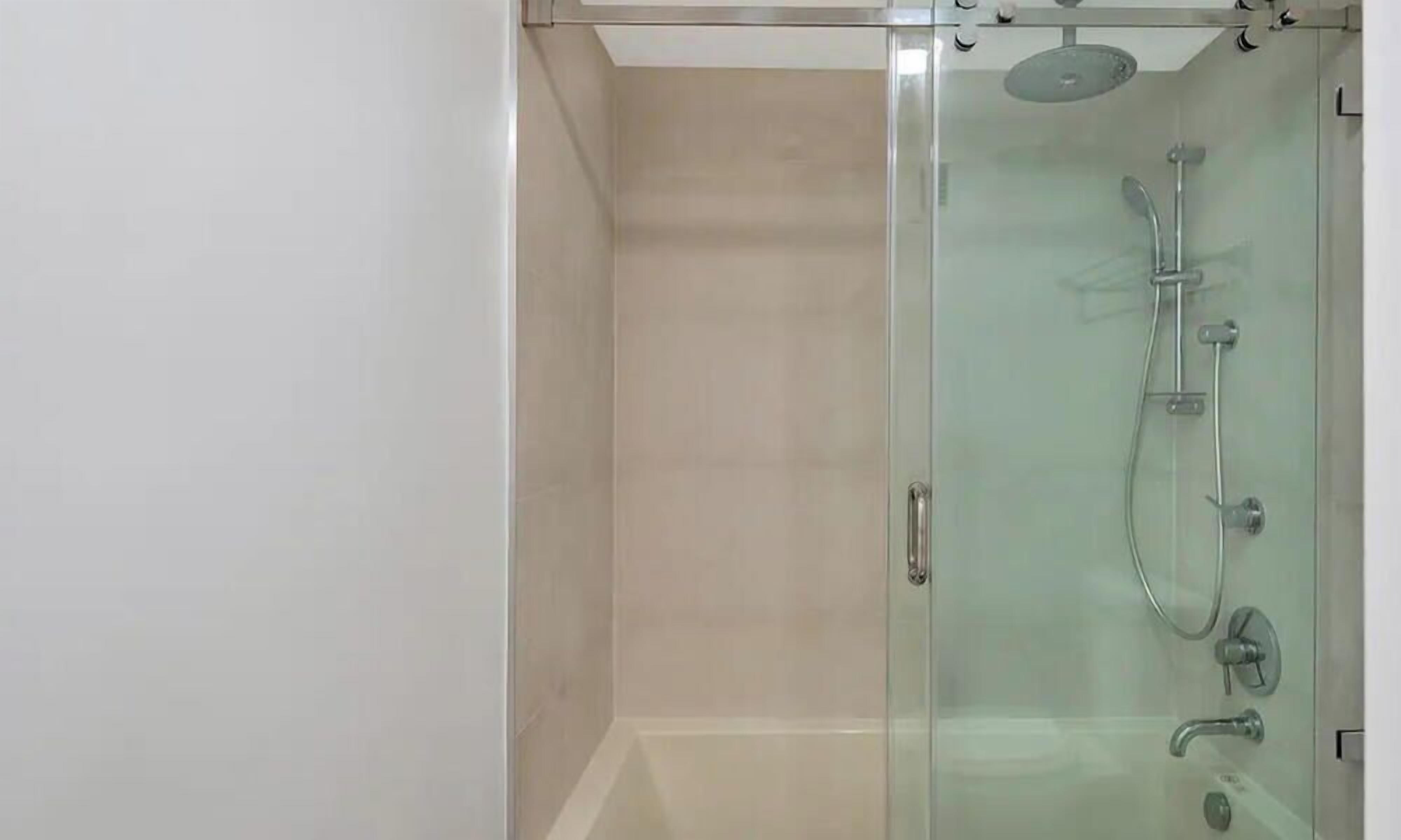 Un área de ducha con paredes de vidrio, un cabezal de ducha manual y un grifo instalado en la pared.