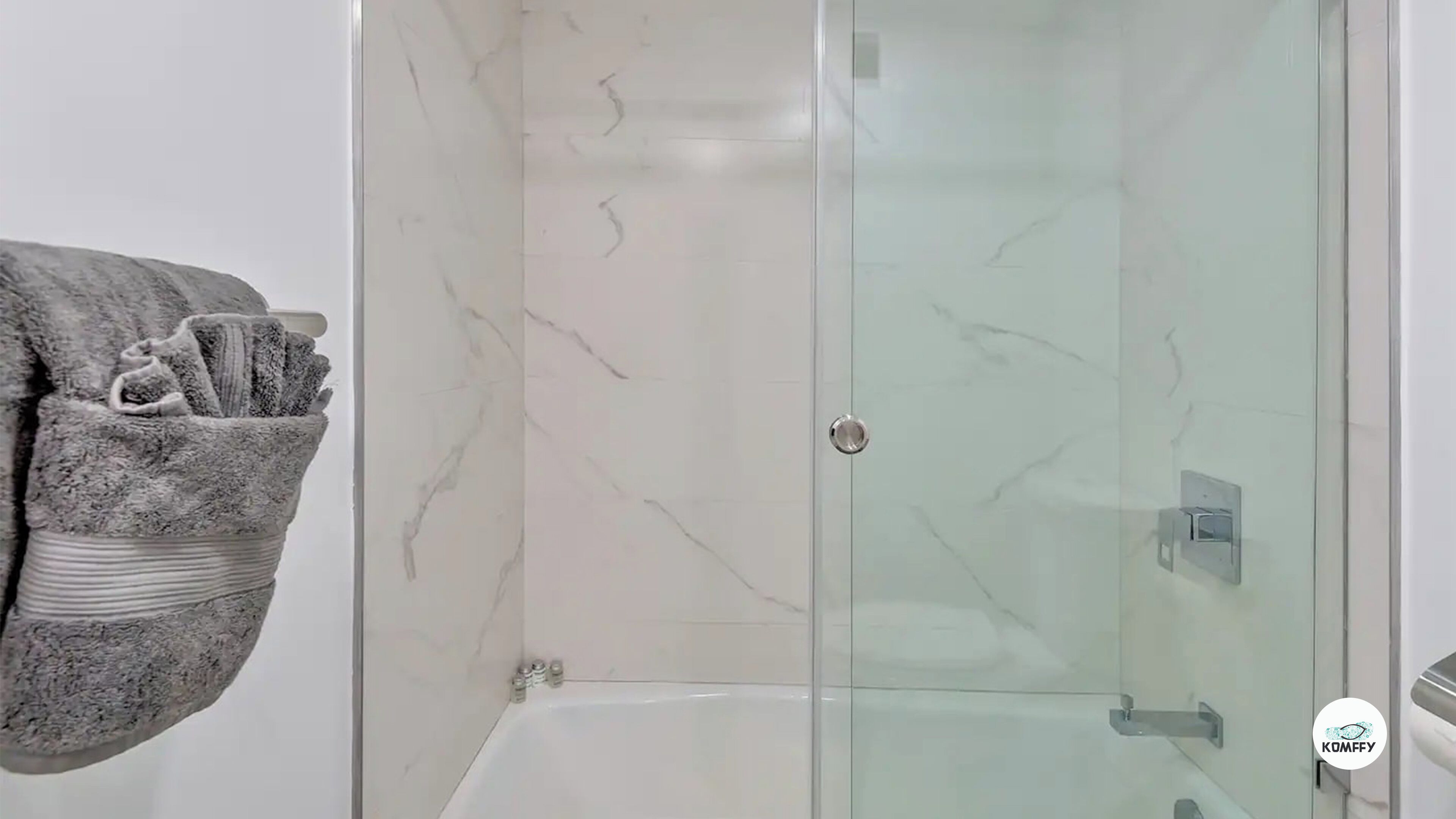 A bathroom with a glass shower enclosure, a marble wall, and a towel rack with a towel and toiletries.