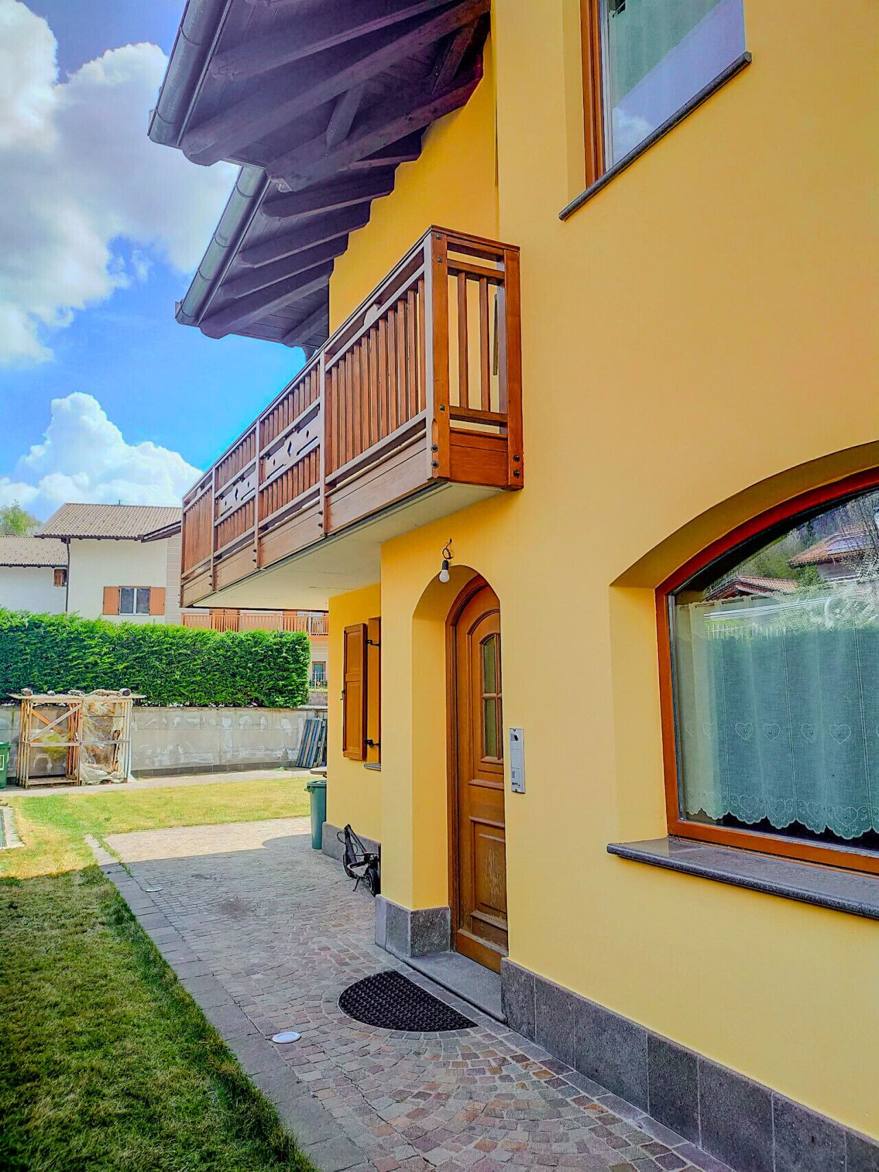 Una casa de dos pisos con un balcón, una puerta de madera y una ventana con cortina.