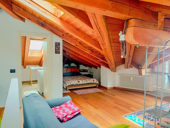 Une chambre mansardée chaleureuse, avec un plafond en pente, un lit superposé, un petit bureau et un radiateur.