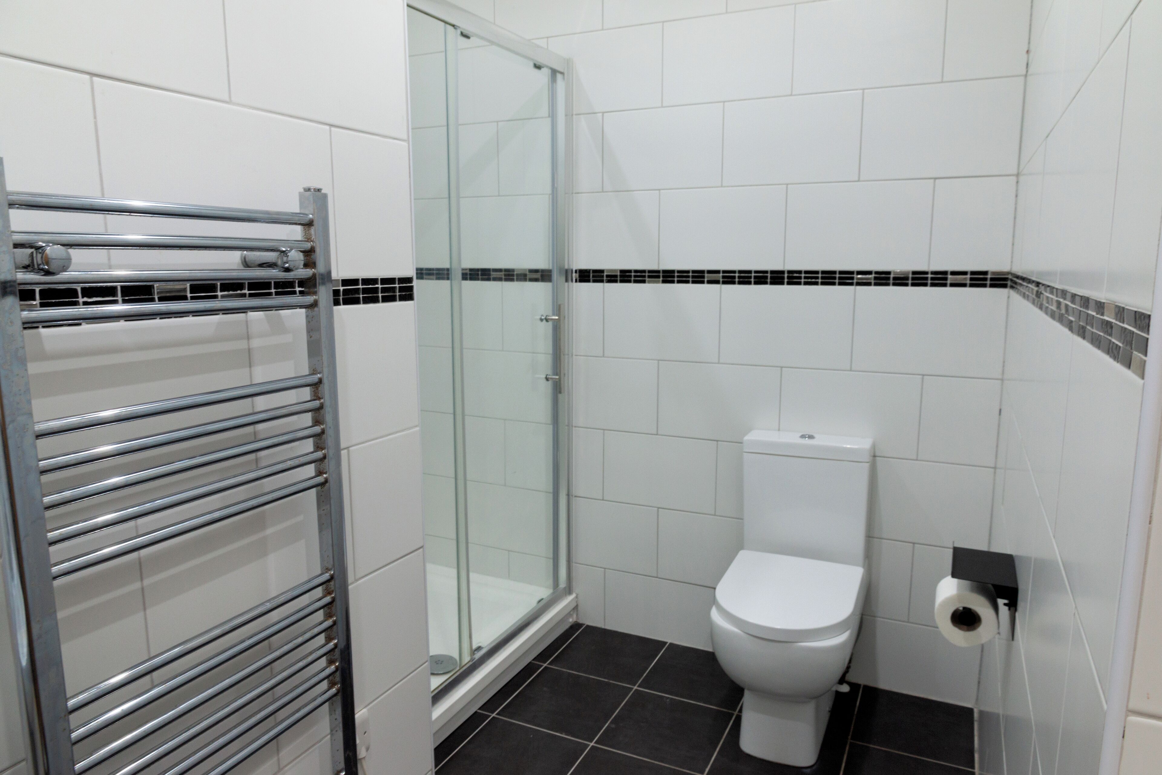A bathroom with a glass shower enclosure, a white toilet, and a metal towel rack.