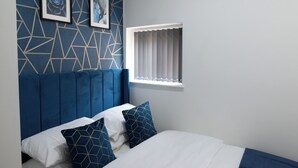 A bedroom with a blue headboard, a bed with white and blue bedding, and two framed pictures on the wall. - Velvet Luxe Retreat Opposite Stadium (Cardiff)