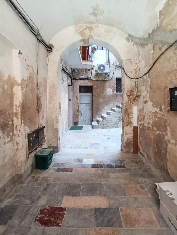 Un couloir étroit au sol carrelé, une porte au fond et un escalier menant à un niveau supérieur.