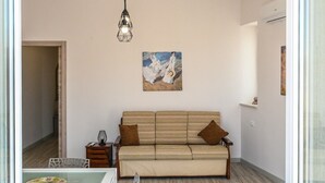 Un salon comprenant un canapé, une table à manger avec des chaises, un luminaire suspendu et un tableau accroché au mur.